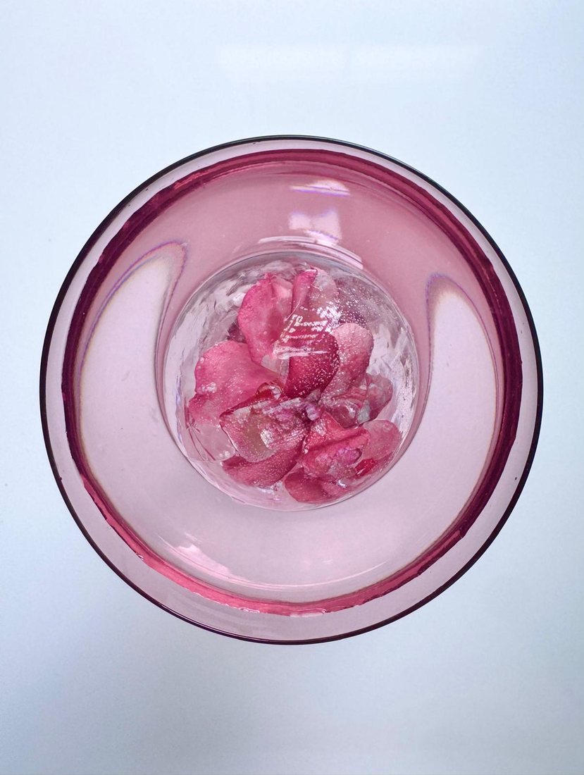 A sphere set with densely-packed rose petals, resting in a fluted pink rocks glass.